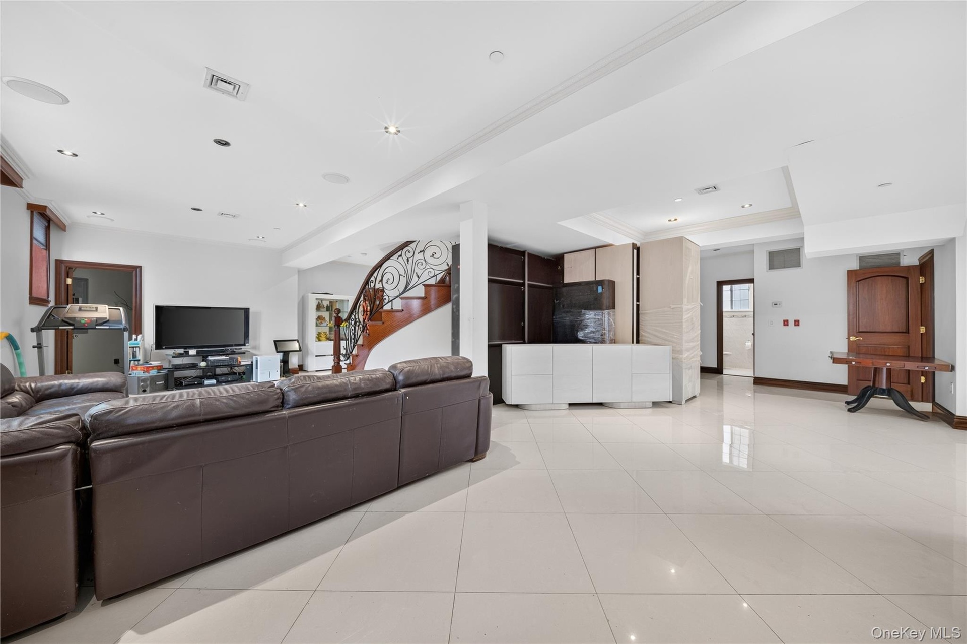 Spacious open-concept room featuring large format tile flooring, recessed lighting, a built-in media cabinet, and a curved staircase with an ornate wr