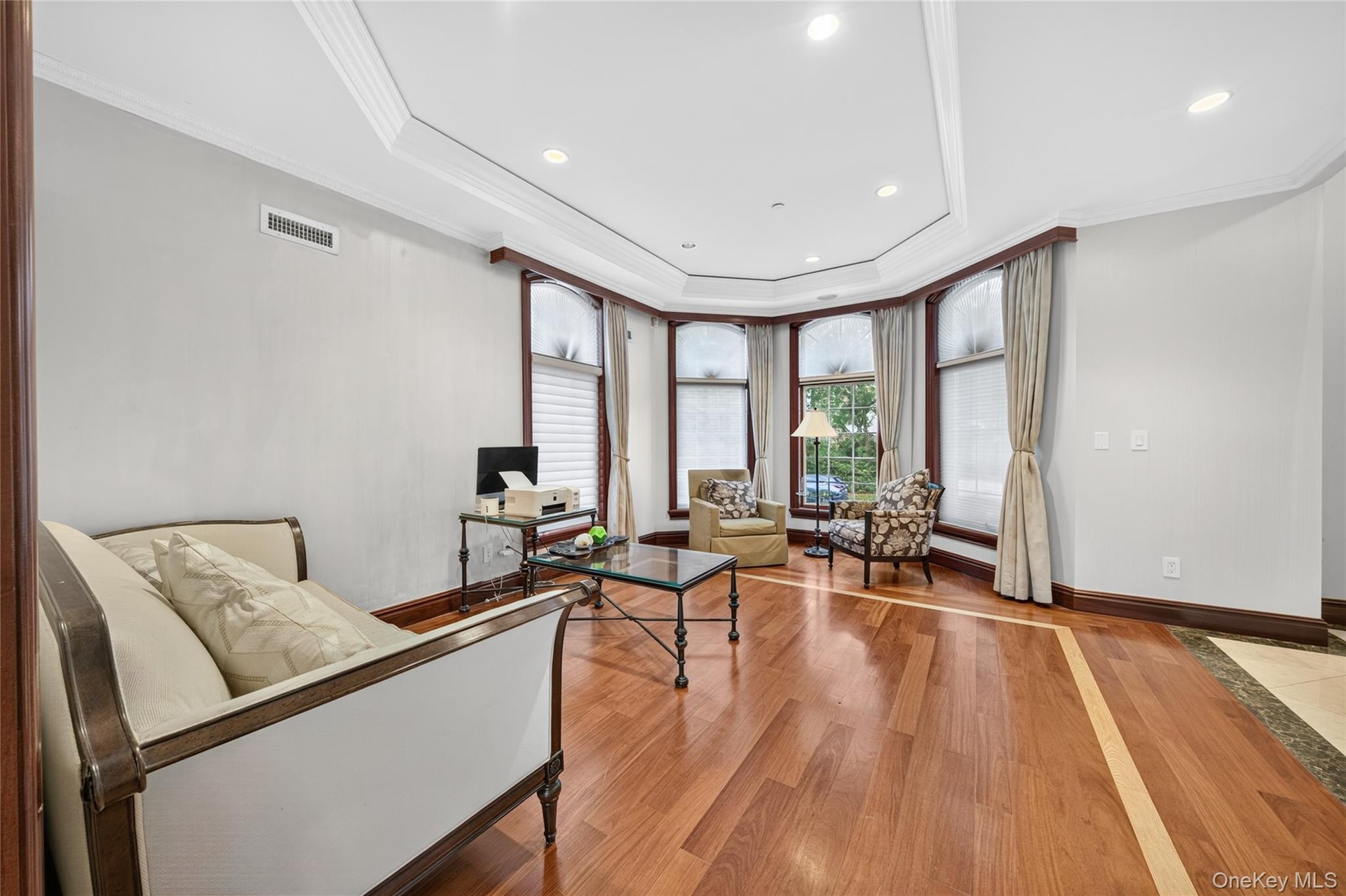 Recessed lighting, crown molding, tray ceiling, hardwood flooring with inlaid detailing, and large bay windows