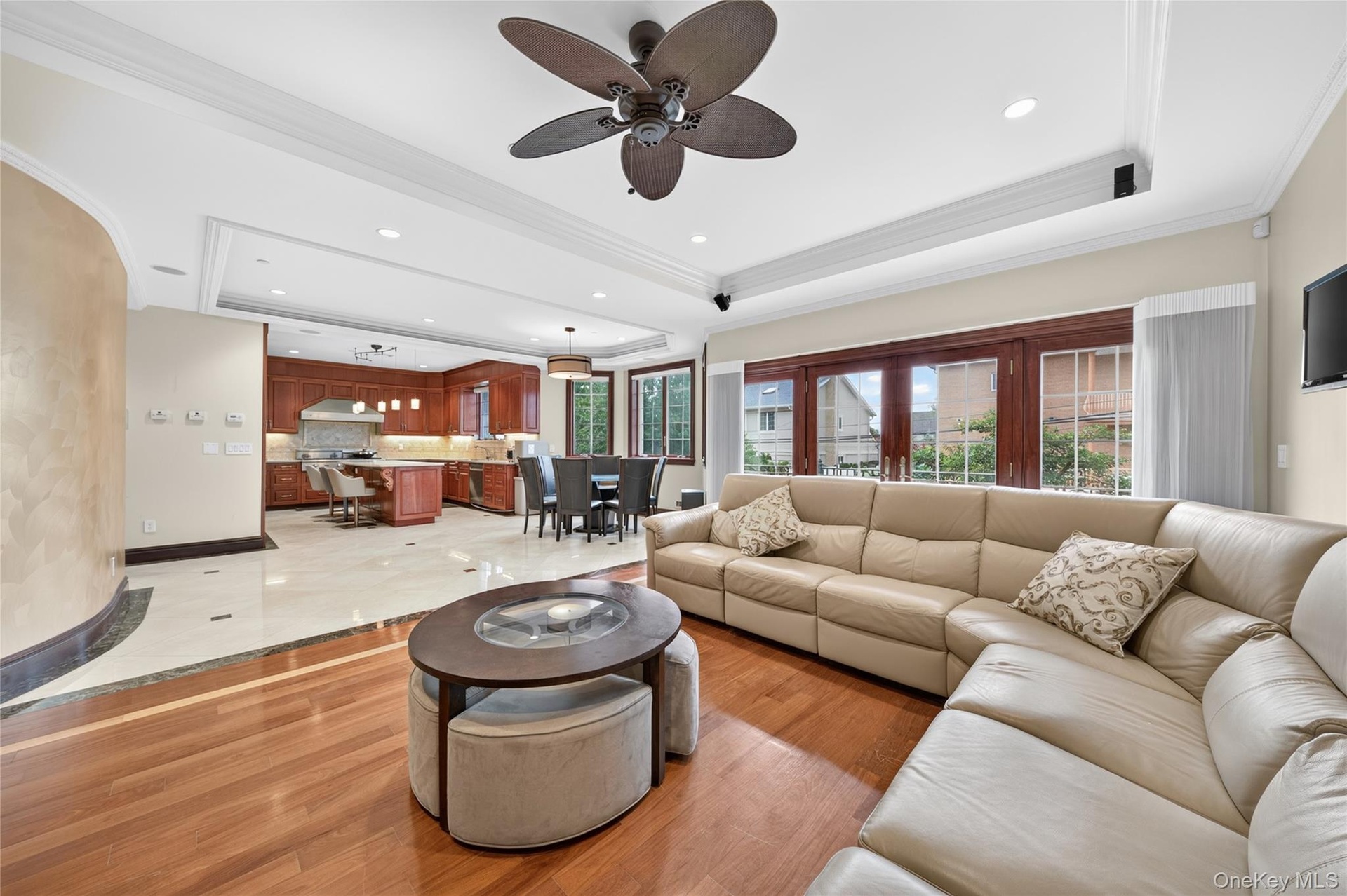 Open-concept living area featuring wood-finish flooring, a tray ceiling with recessed lighting, and a ceiling fan