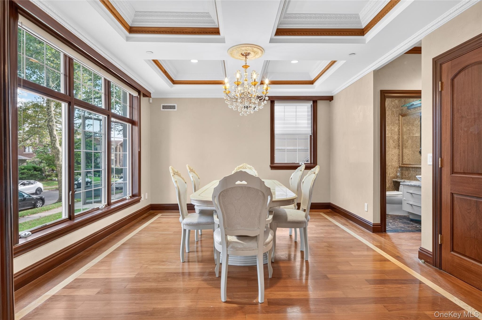 Hardwood flooring with inlay, extensive wood trim, multiple large windows, coffered ceiling, and a crystal chandelier
