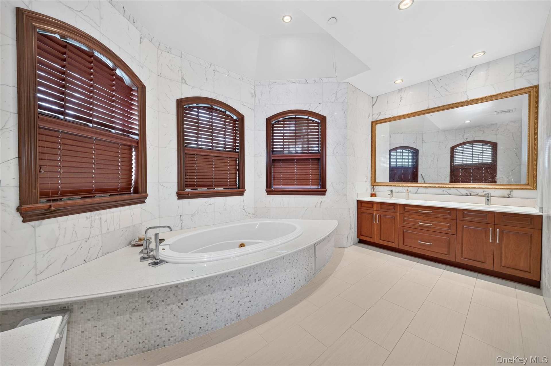 Integrated soaking tub with deck, dual vanities with undermount sinks, large wall mirror, and tiled walls