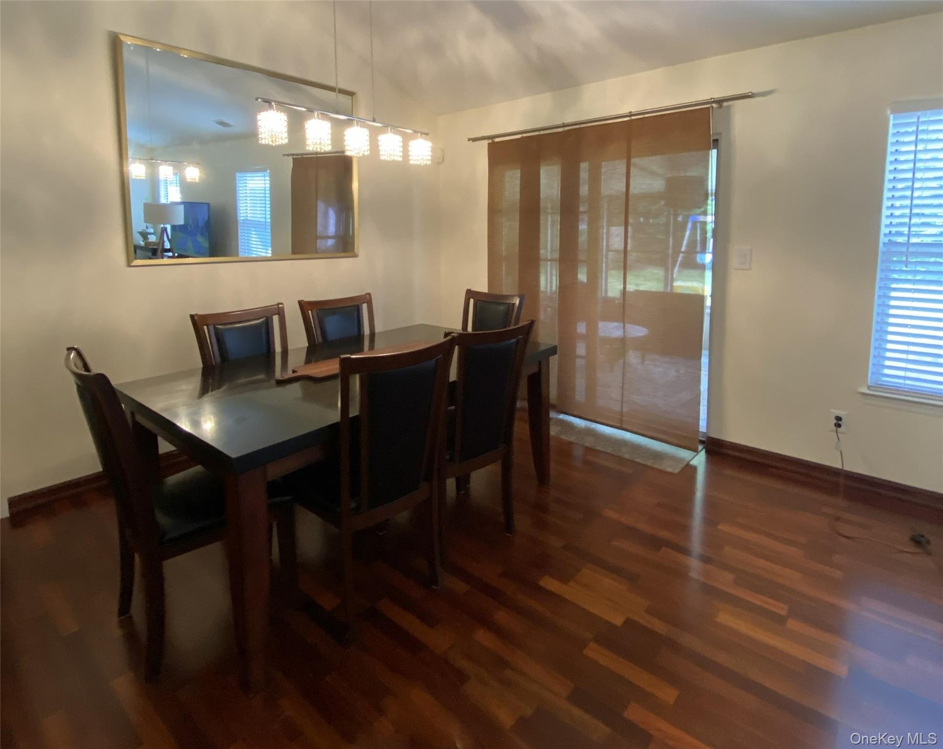 Wood-finish flooring throughout, with a framed wall mirror and overhead linear chandelier
