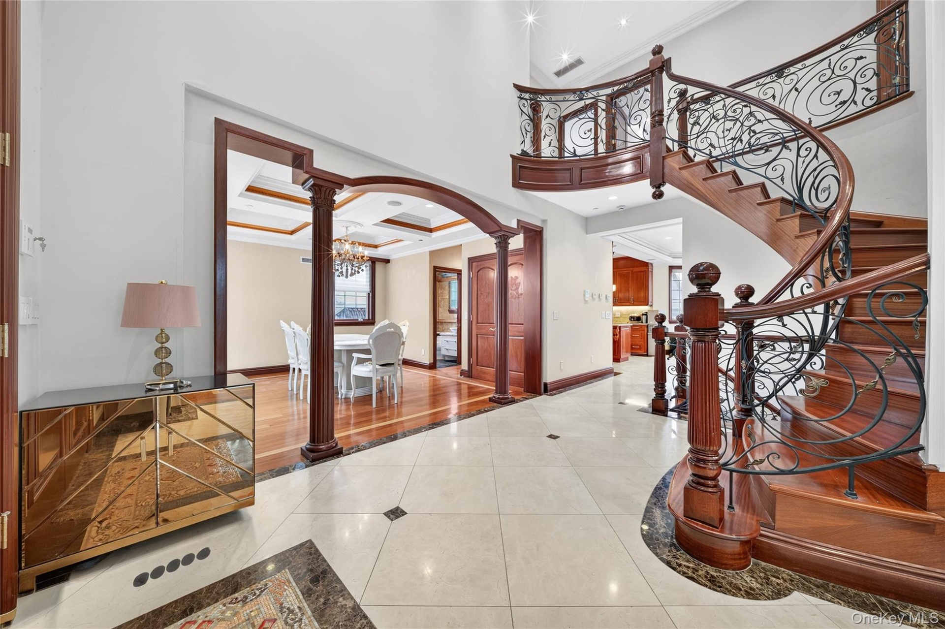 Grand entryway featuring a curved staircase with ornate ironwork and wood-finish treads, a coffered ceiling, and a formal dining space with hardwood f