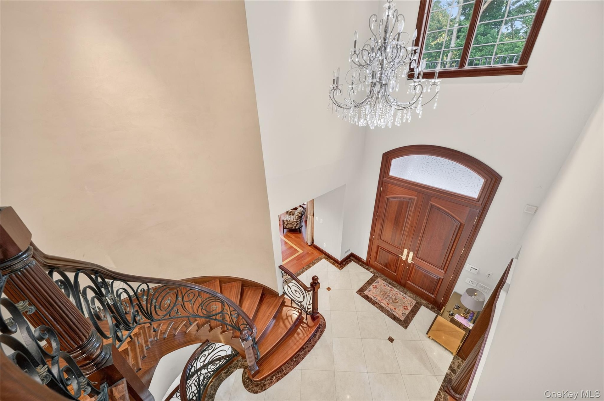 Grand foyer featuring a crystal chandelier, arched double entry doors, a large transom window, a curved staircase with an ornate wrought iron railing,