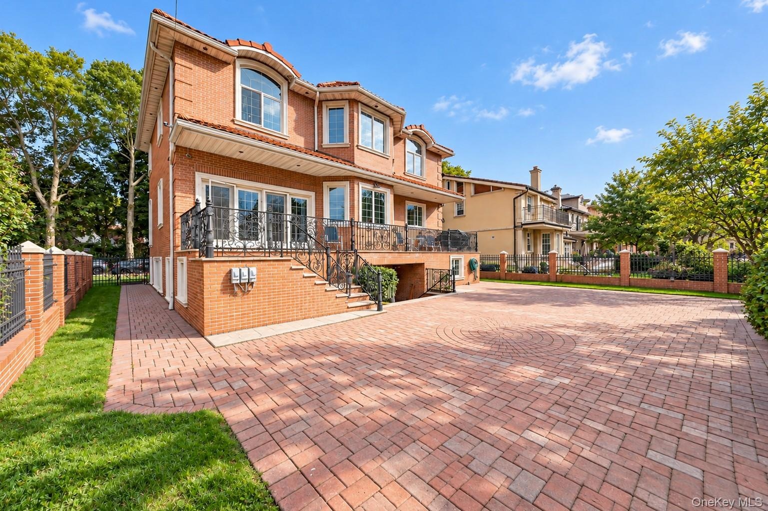 Brick exterior with a tile roof, featuring a paver driveway, wrought iron balcony, and a brick privacy wall with iron fencing