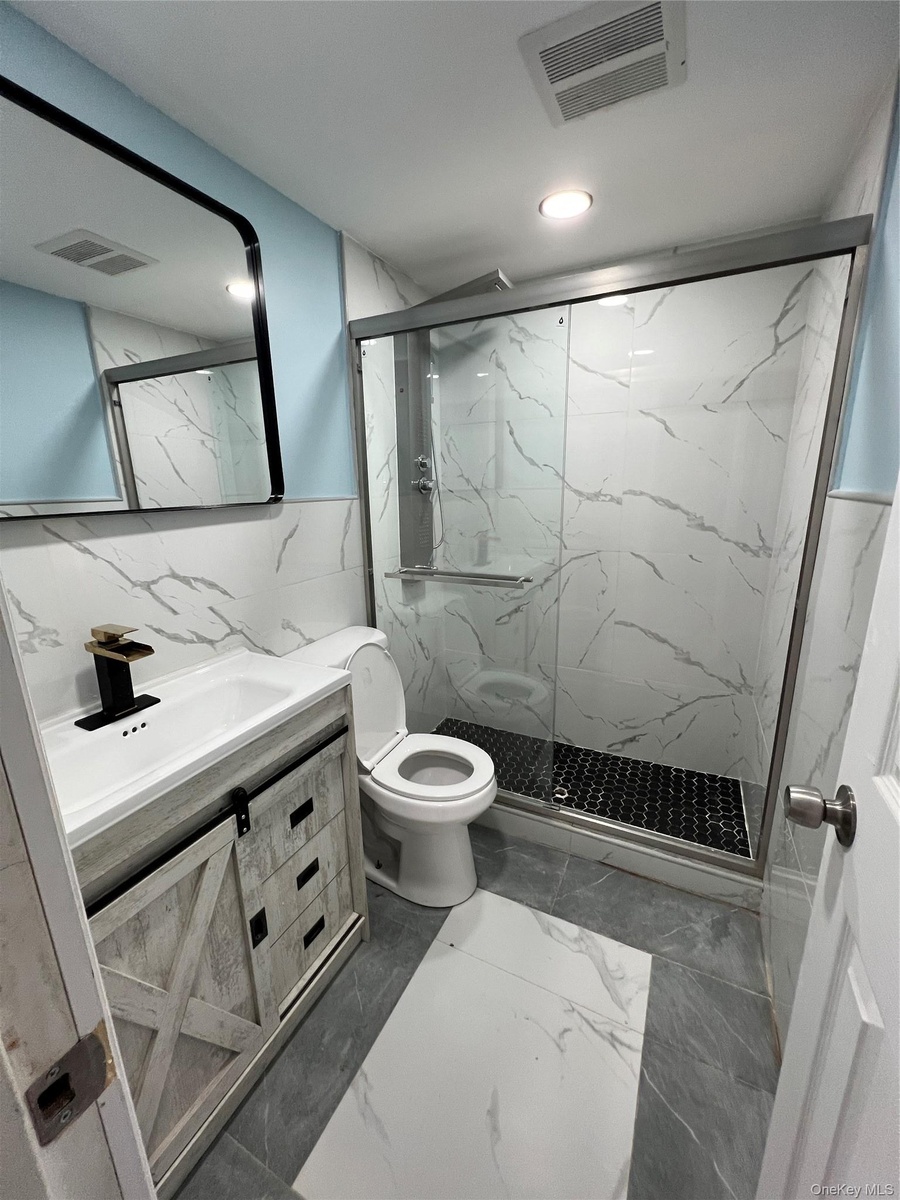 Modern basement bathroom featuring a glass enclosed shower with black hexagonal tile flooring and white marbled wall tile