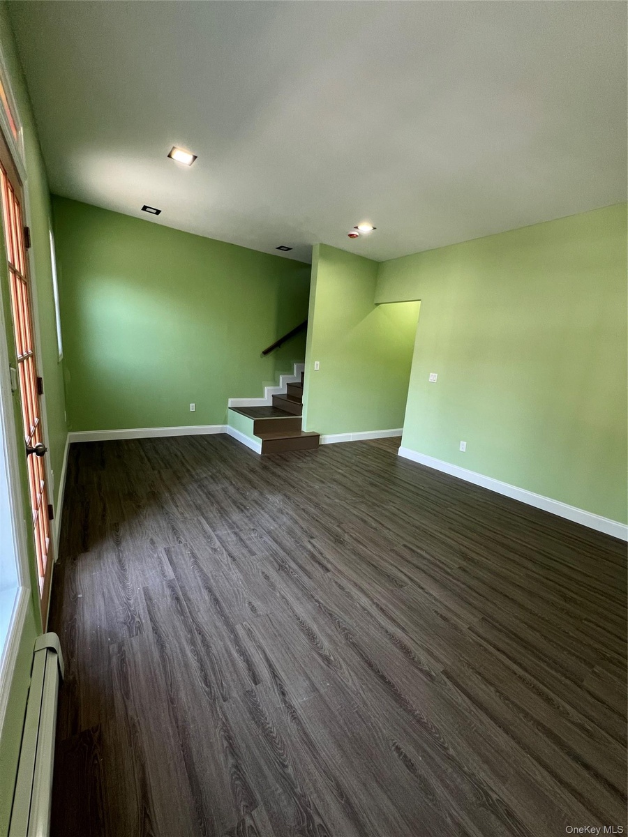 Spacious area featuring wood-finish flooring, recessed lighting, and a staircase with a dark handrail