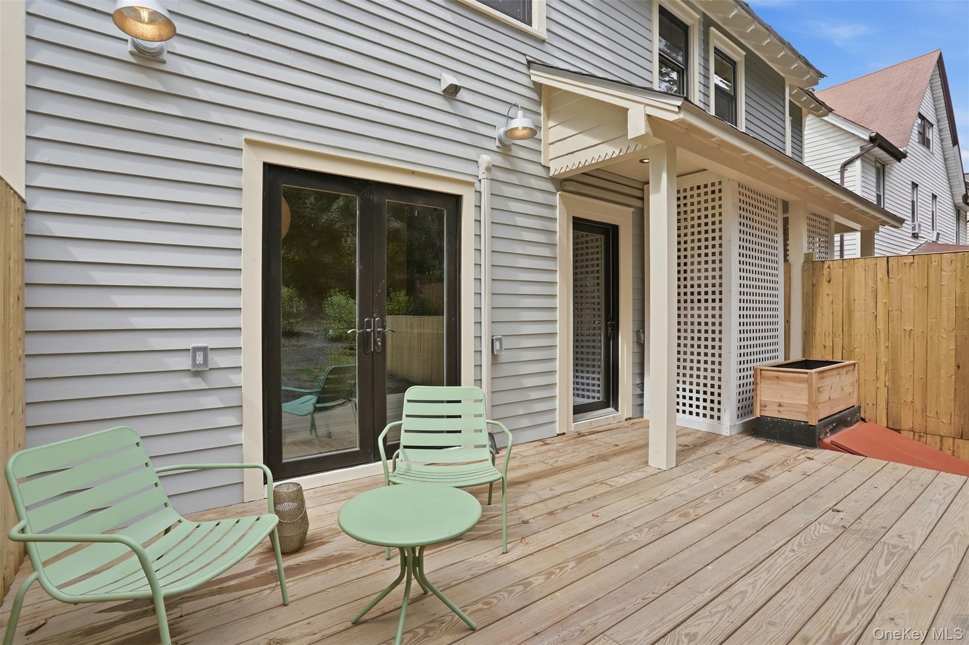 Expansive wood deck with light gray siding, privacy fencing, and dual exterior light fixtures