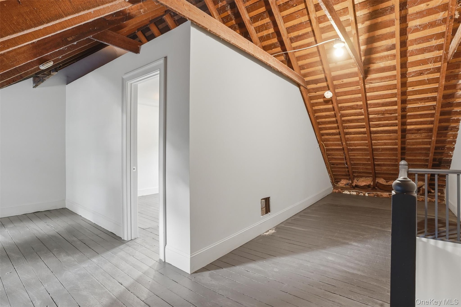 Exposed wood rafter ceiling, painted wood flooring, white painted walls, and an interior doorway