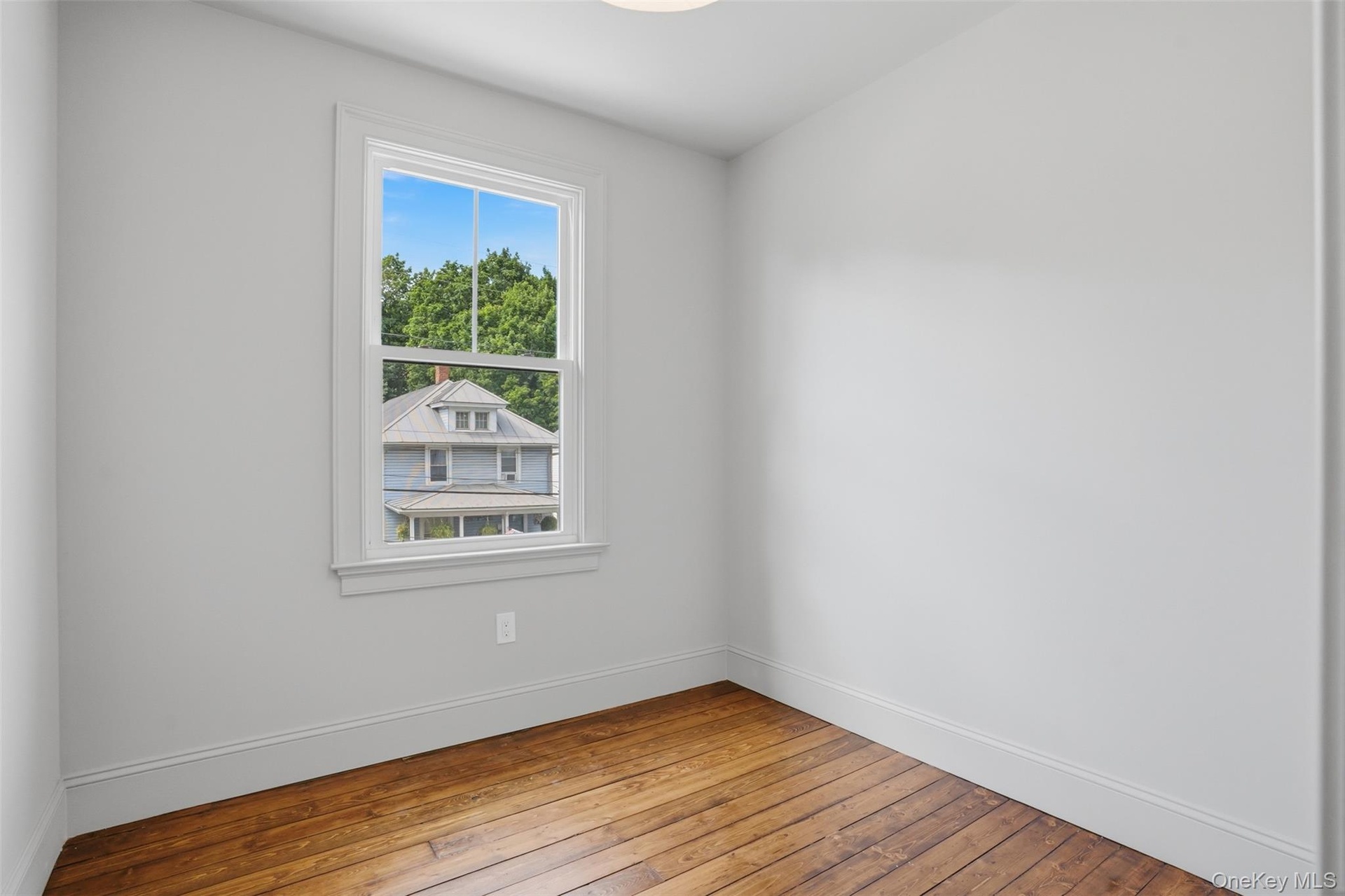 Hardwood flooring, painted walls, window with white trim, and a ceiling-mounted light fixture