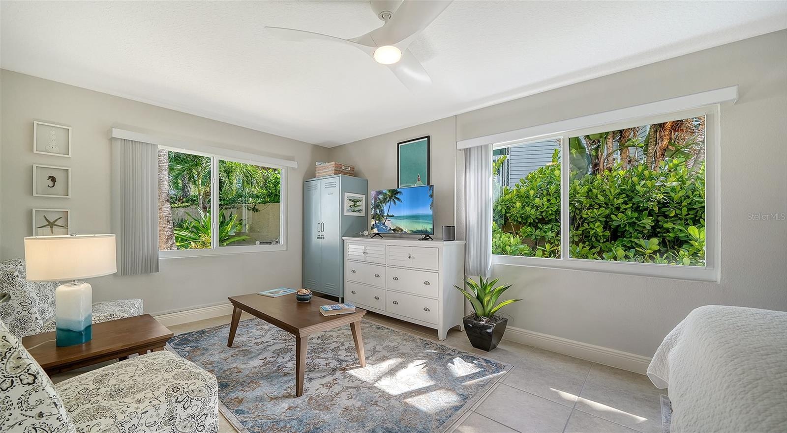 Bright guest bedroom with multiple windows overlooking the lush landscaping.