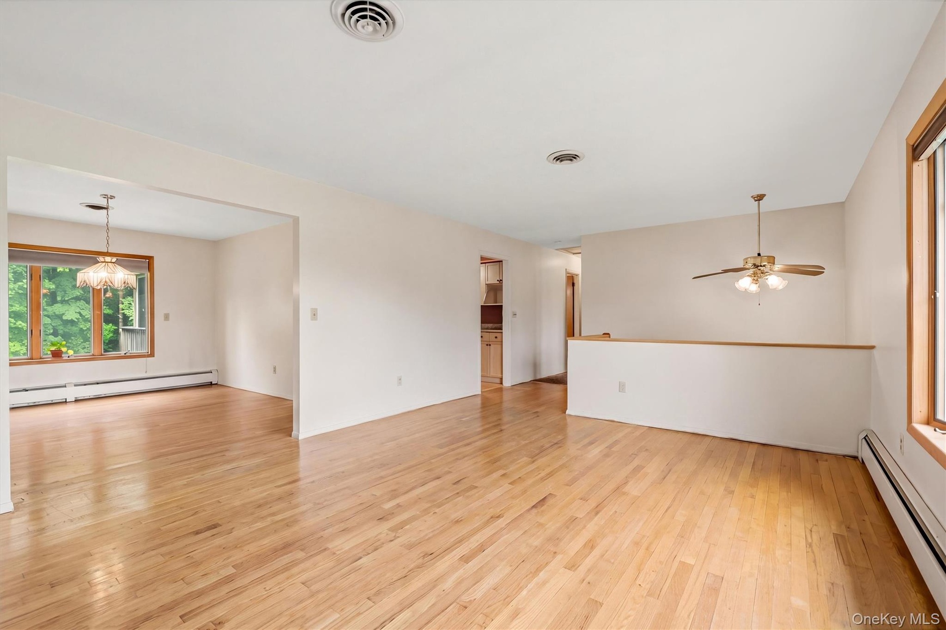 Hardwood flooring throughout, with a semi-open floor plan, a ceiling fan with integrated lighting, and  large windows