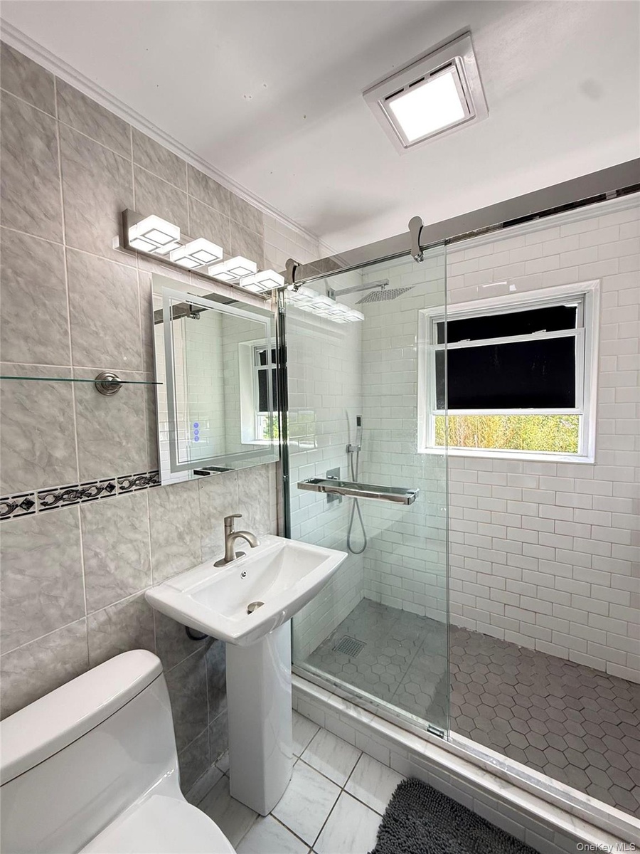 Pedestal sink, wall-mounted vanity lighting, frameless glass shower enclosure, subway tile shower surround, and hexagonal tile shower floor