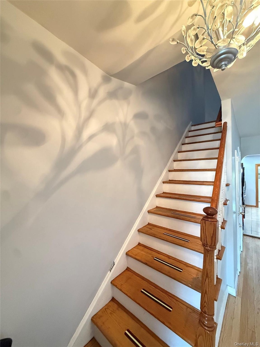 Natural wood treads with integrated non-slip strips, white risers, and a wood banister, illuminated by a decorative chandelier