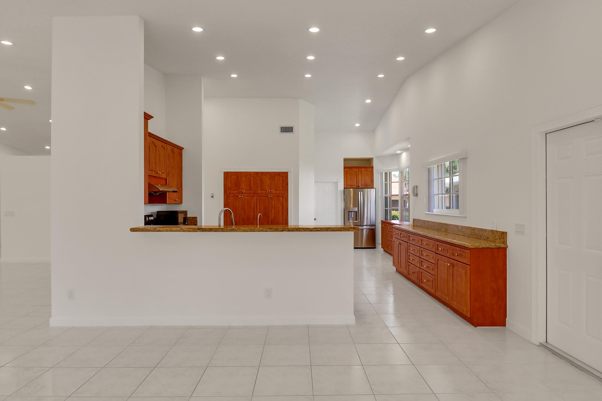 Kitchen and living area featuring white tile flooring, vaulted ceilings, recessed lighting, wood cabinetry, and stainless steel appliances