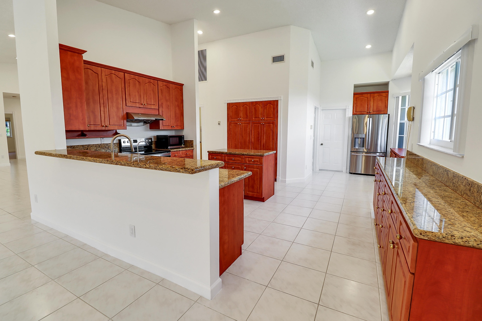 Open-concept kitchen featuring wood cabinetry, light-toned tiled flooring, and vaulted ceilings with recessed lighting