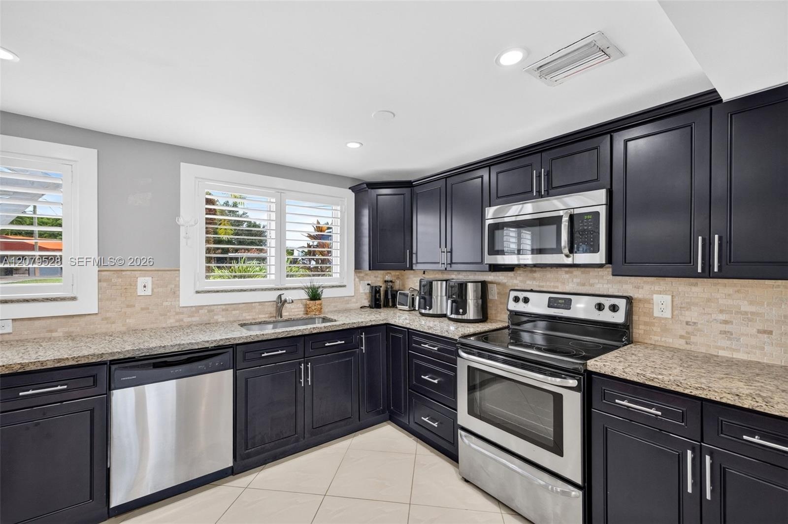 Large bright kitchen w/ windows everywhere, plantation shutters, wood cabinets, stainless appliances and granite counters