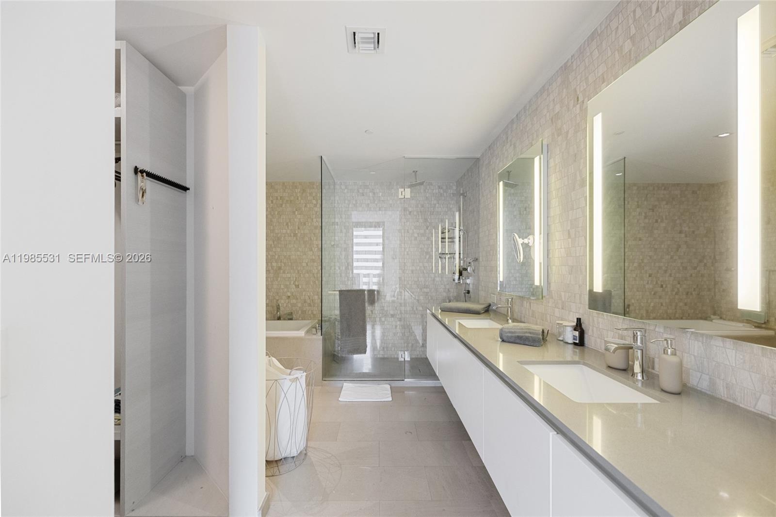Bathroom featuring textured stone mosaic wall tile, a frameless glass-enclosed shower, a deep soaking tub with a stone surround, and a wall-mounted to