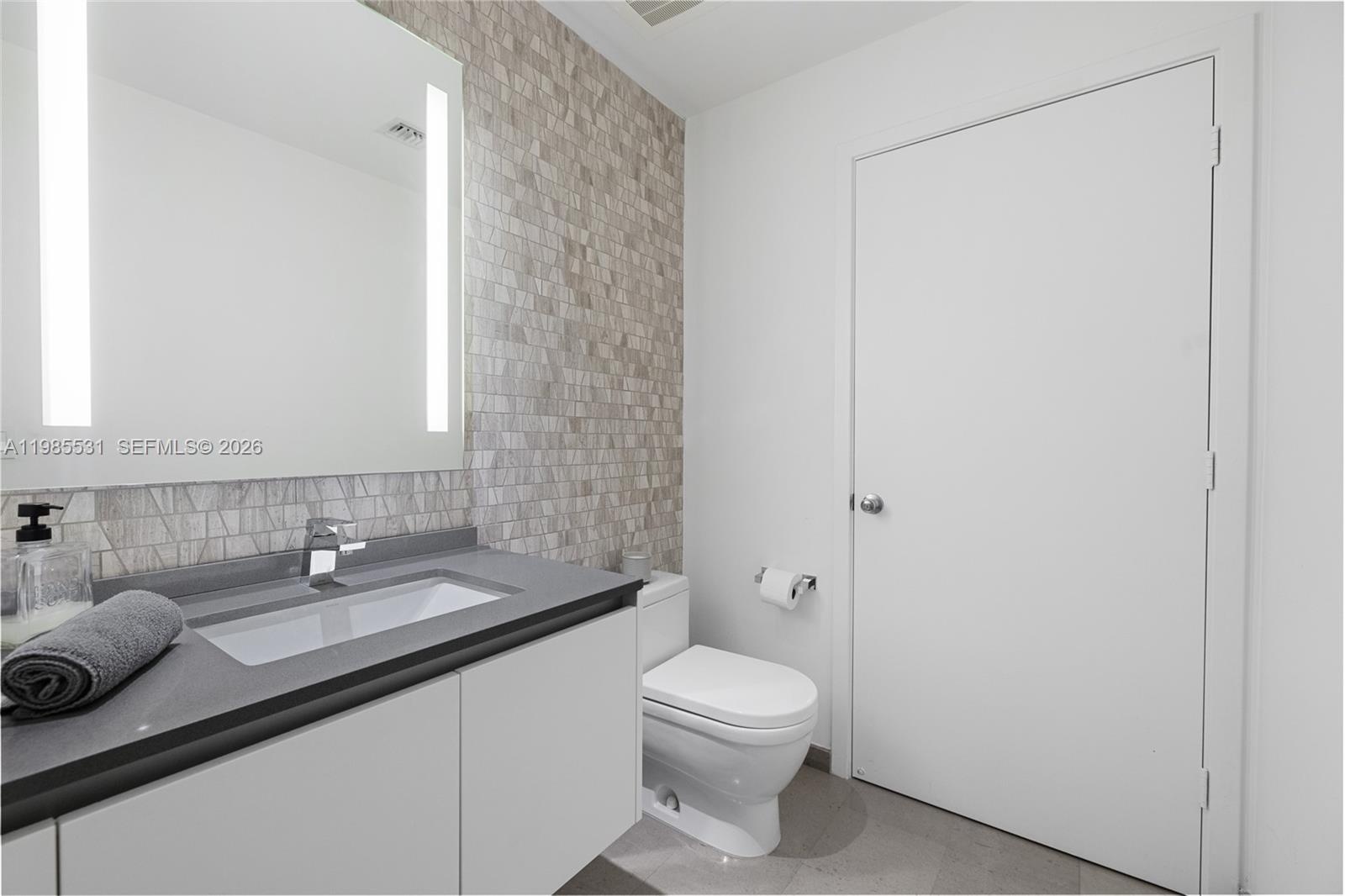 Large-format gray wood-finish door with brushed metal hardware, neutral stone flooring, and white louvered door