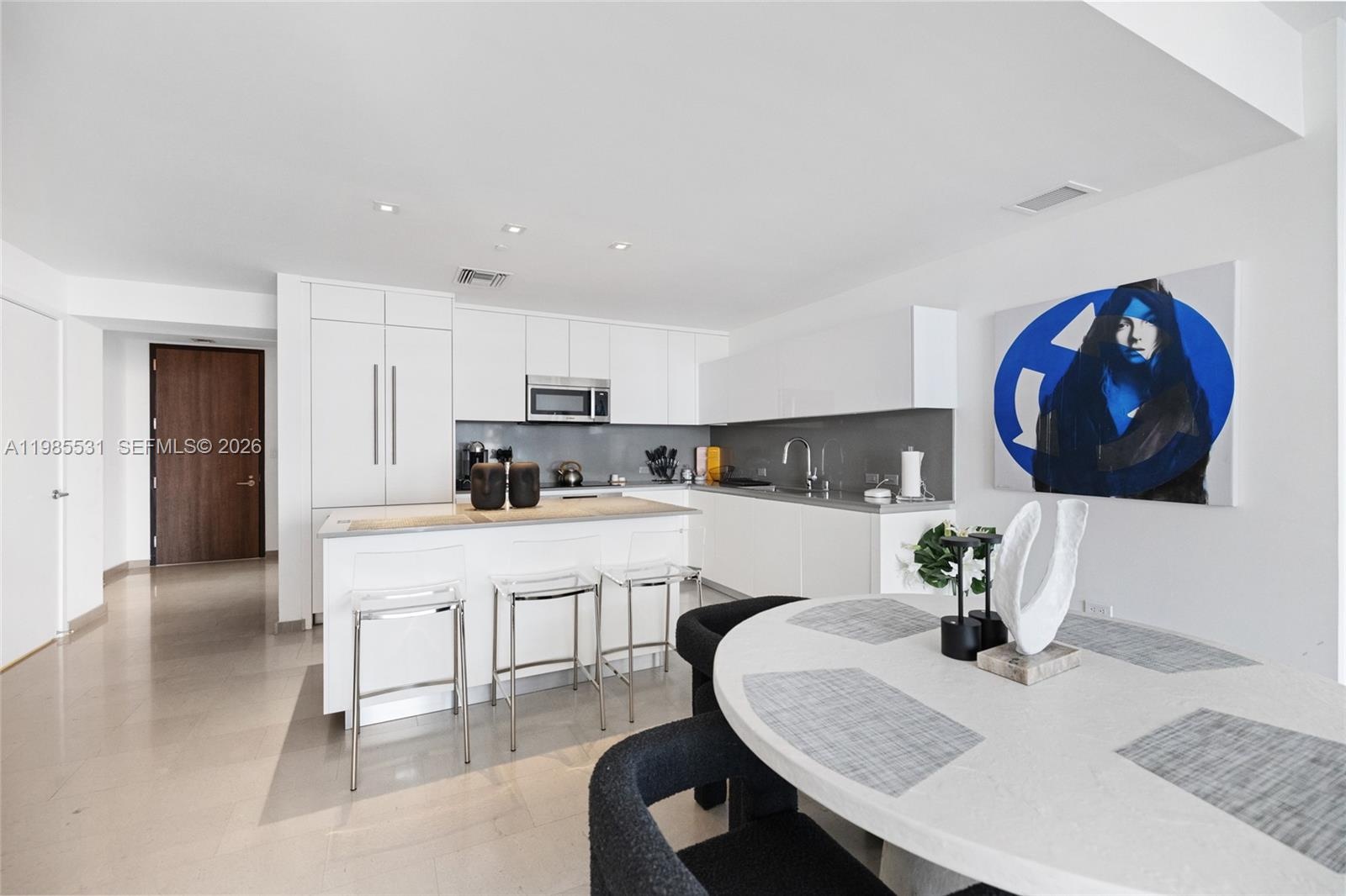 Neutral-toned stone flooring throughout, smooth white wall finishes, and a solid-core door featuring a louvered panel