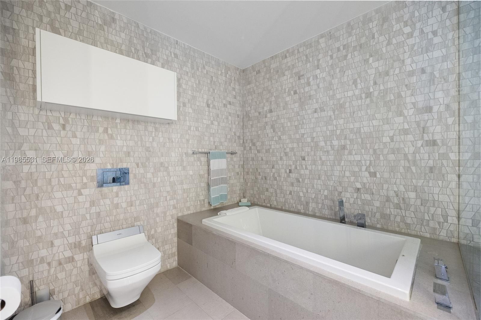 Walk-in shower featuring glass paneling, floor-to-ceiling mosaic tile surround, and wall-mounted plumbing fixtures, accompanied by a white floating va