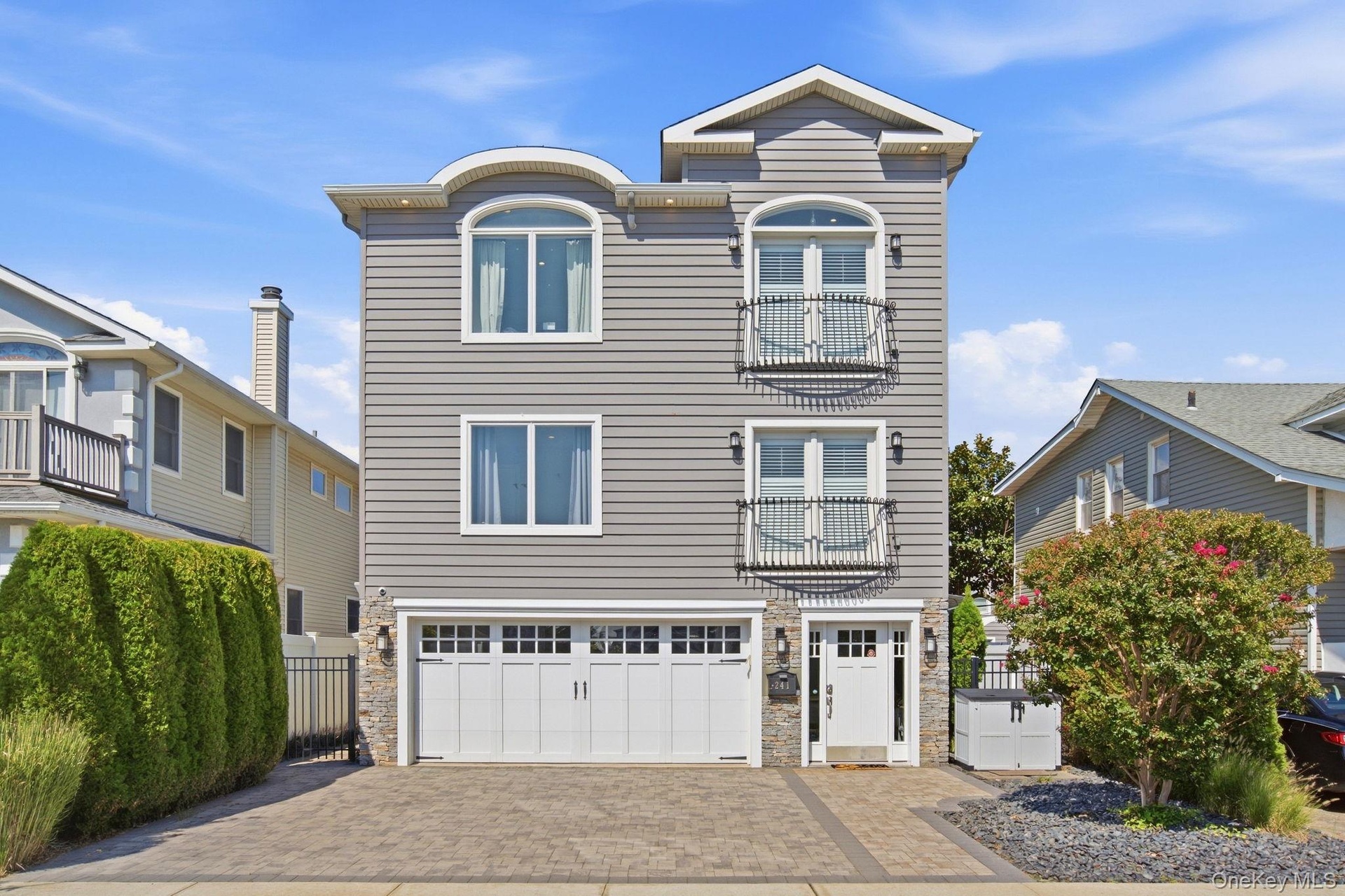 Three-story home with stone accents, featuring a paver driveway, and Juliette balconies