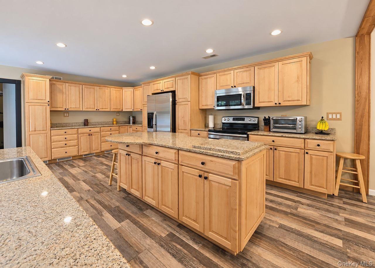 Spacious kitchen featuring extensive light wood cabinetry, stone countertops, a large center island, wood-finish flooring, and recessed lighting