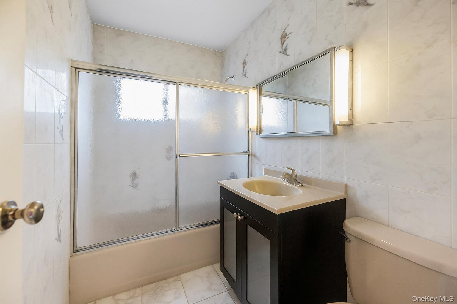 Full bathroom featuring enclosed tub / shower combo, vanity, and tile walls