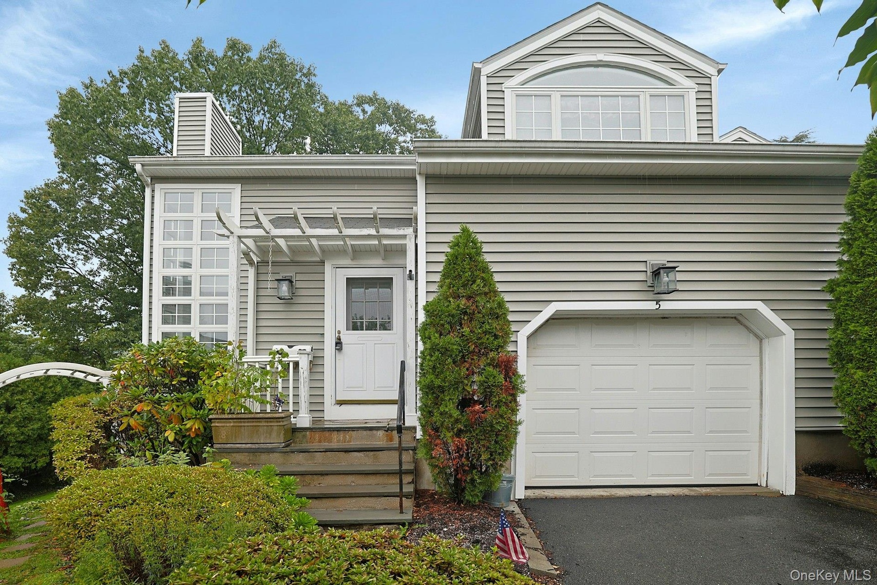 Siding exterior with a paneled garage door, arched window, and a white front entry door with an overhead pergola