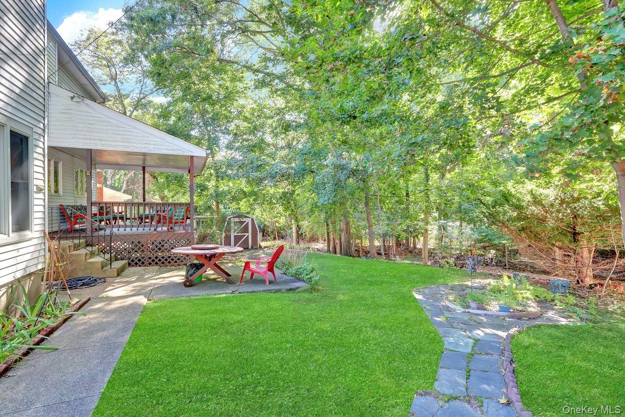 Expansive backyard featuring a manicured lawn, established trees, and a covered porch with a wood railing