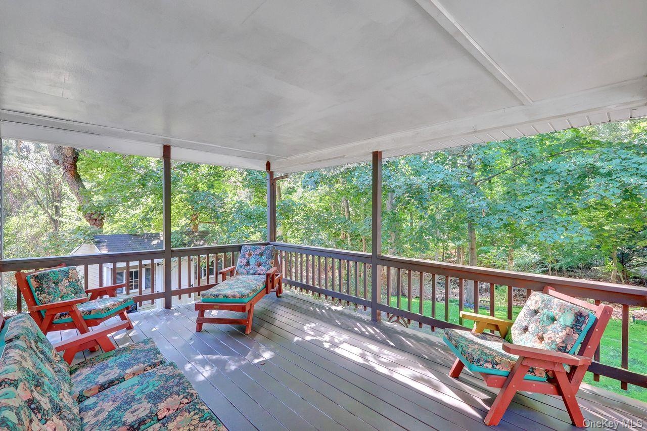 Covered outdoor deck with wood flooring and dark wood railings, surrounded by mature trees