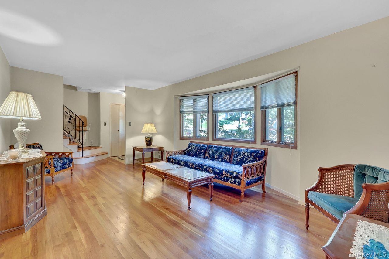 Hardwood flooring throughout, bay window with multiple panes, staircase with ornamental metal railing, and neutral wall tones