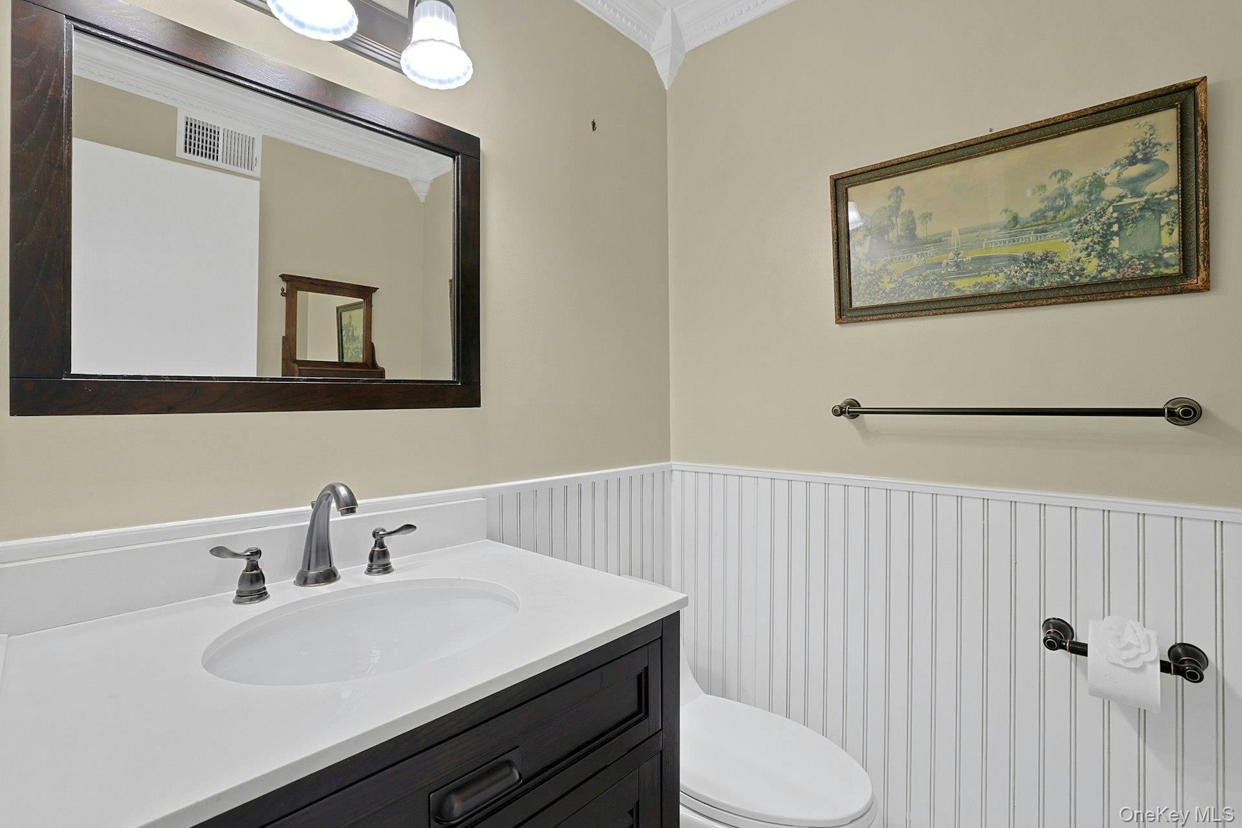 The updated hall half bathroom on the first floor features wainscotting, crown molding and a Corian vanity with a beautiful tri-fixture light.