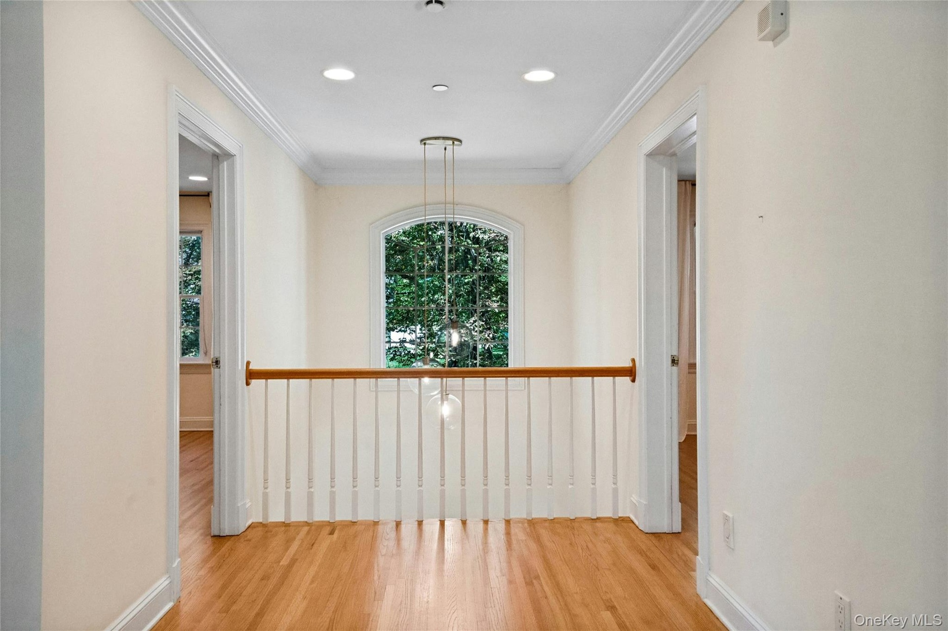 Balcony over looking the living room on one side and the foyer on the other.  Hardwood flooring, crown molding, recessed lighting, arched window, and 