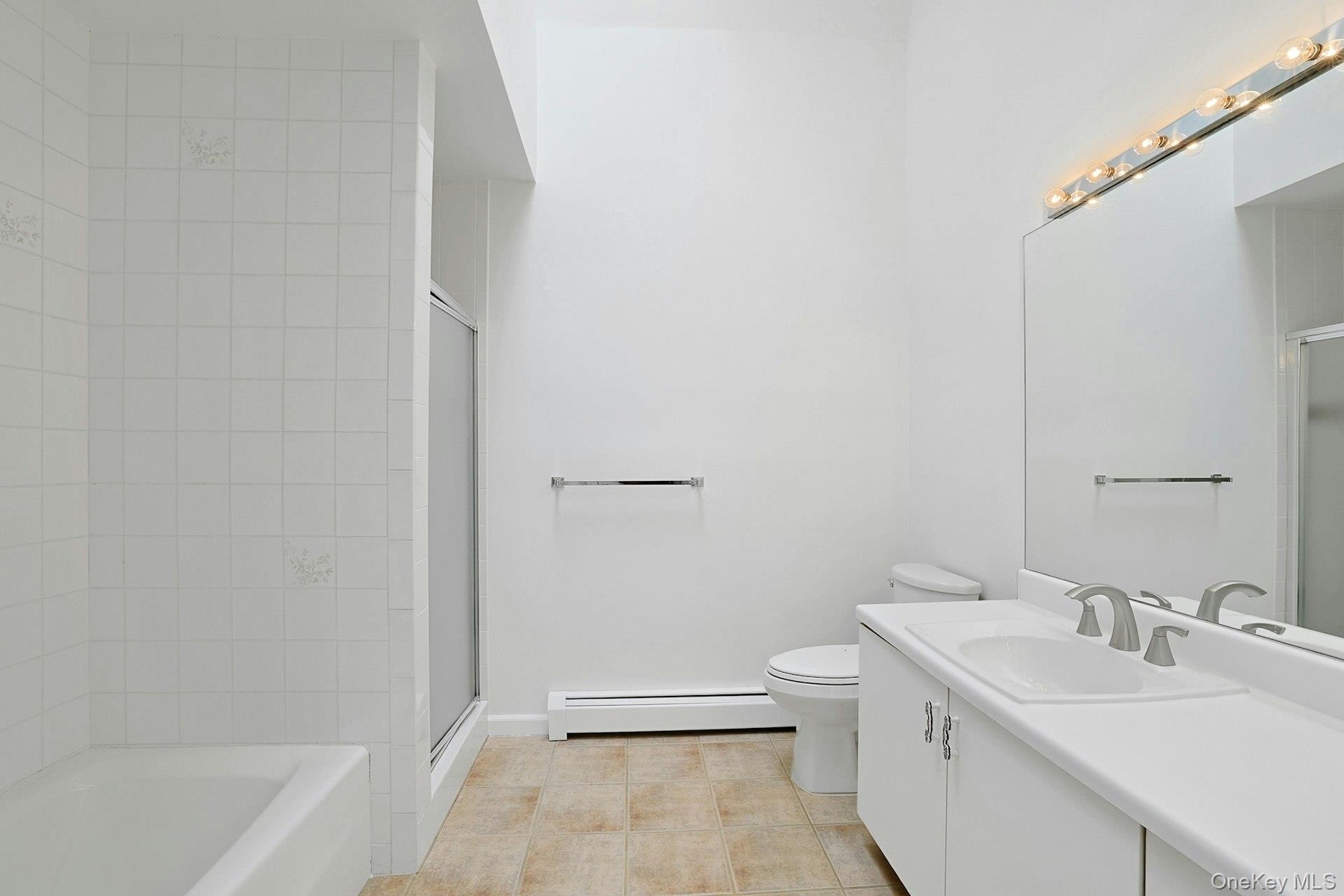 The primary bathroom, with tiled floor and a high ceiling that rises up to a skylight, is a private oasis. The long vanity is very usable, and there i