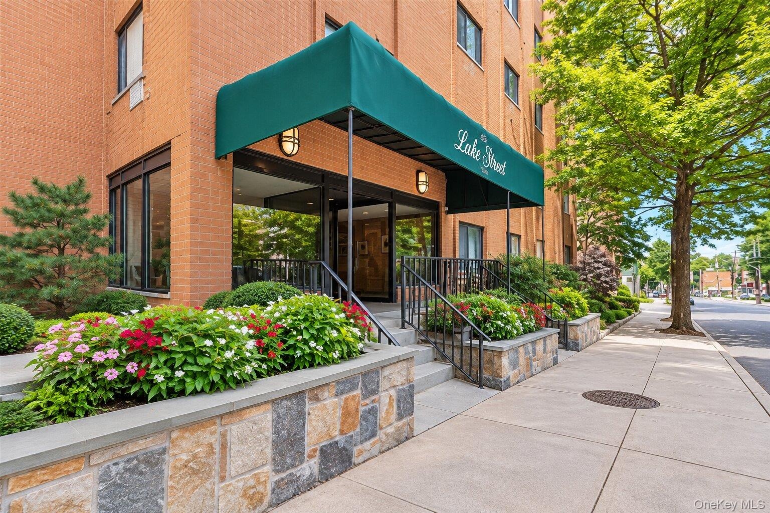 Brick facade building featuring a green awning, stone-clad planters, wrought iron railings, and extensive landscaping