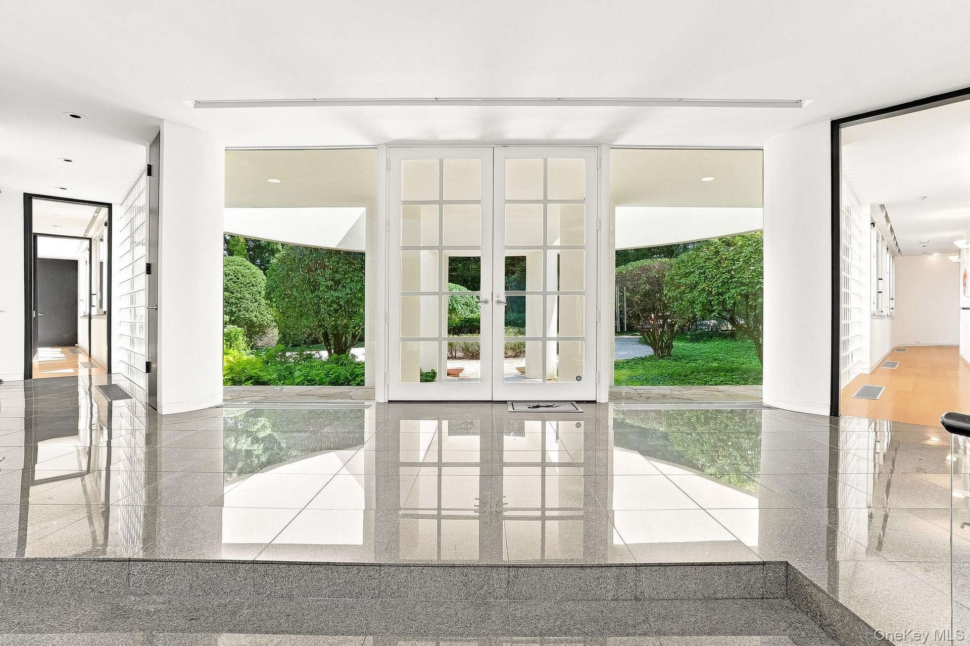 Polished granite-style tile floors and expansive floor-to-ceiling windows flood this striking modern foyer with lush green views.