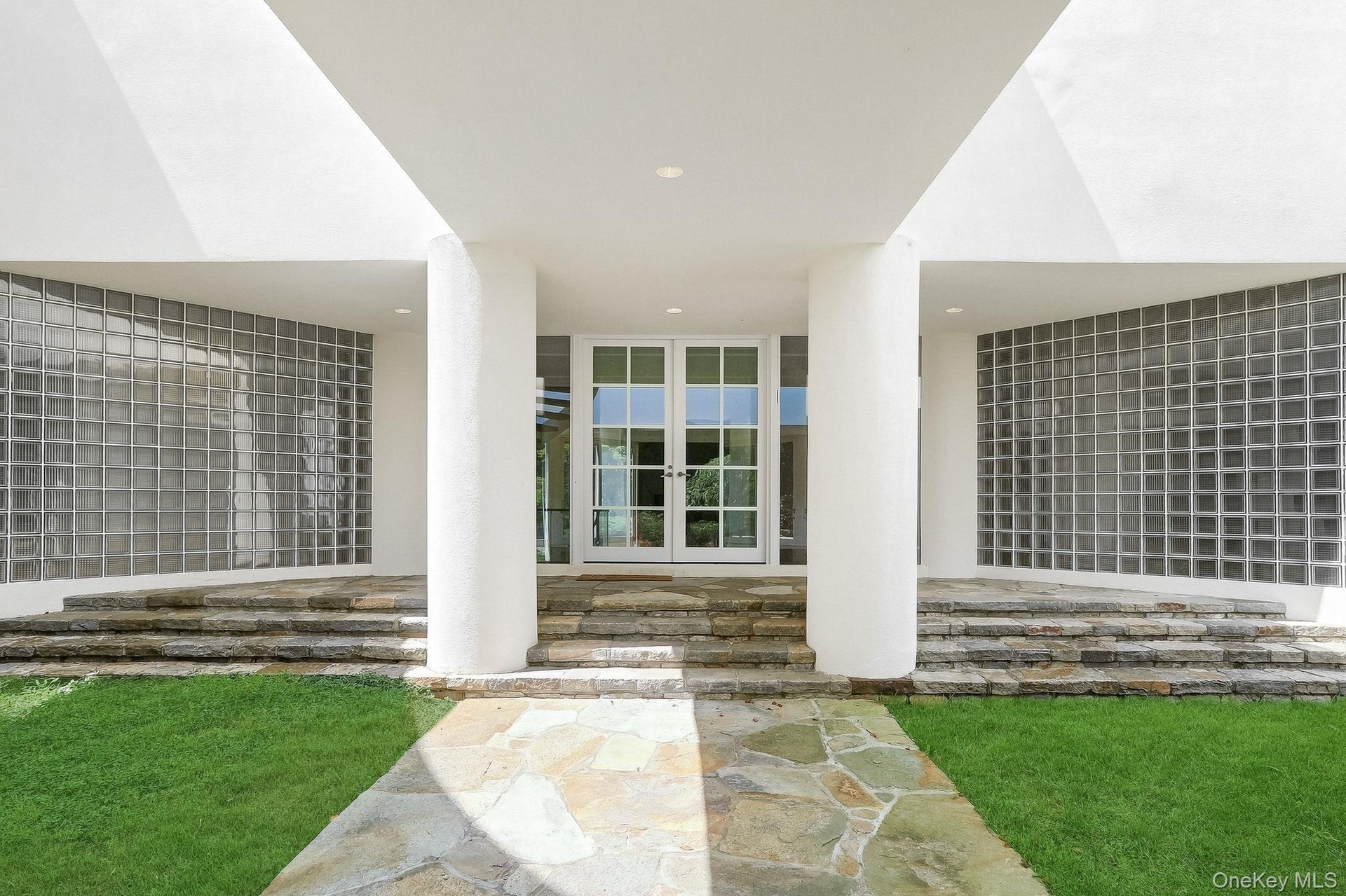 Oversized columns and elegant glass double doors frame a spectacular modern entry framed by curved glass-block privacy walls.