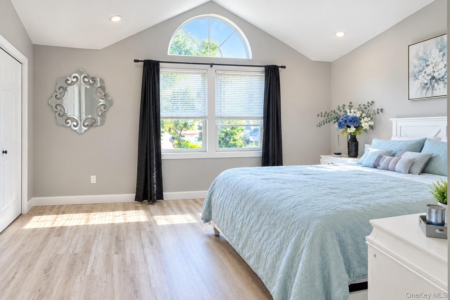 Vaulted ceiling with an arched window, finished flooring, and recessed lighting