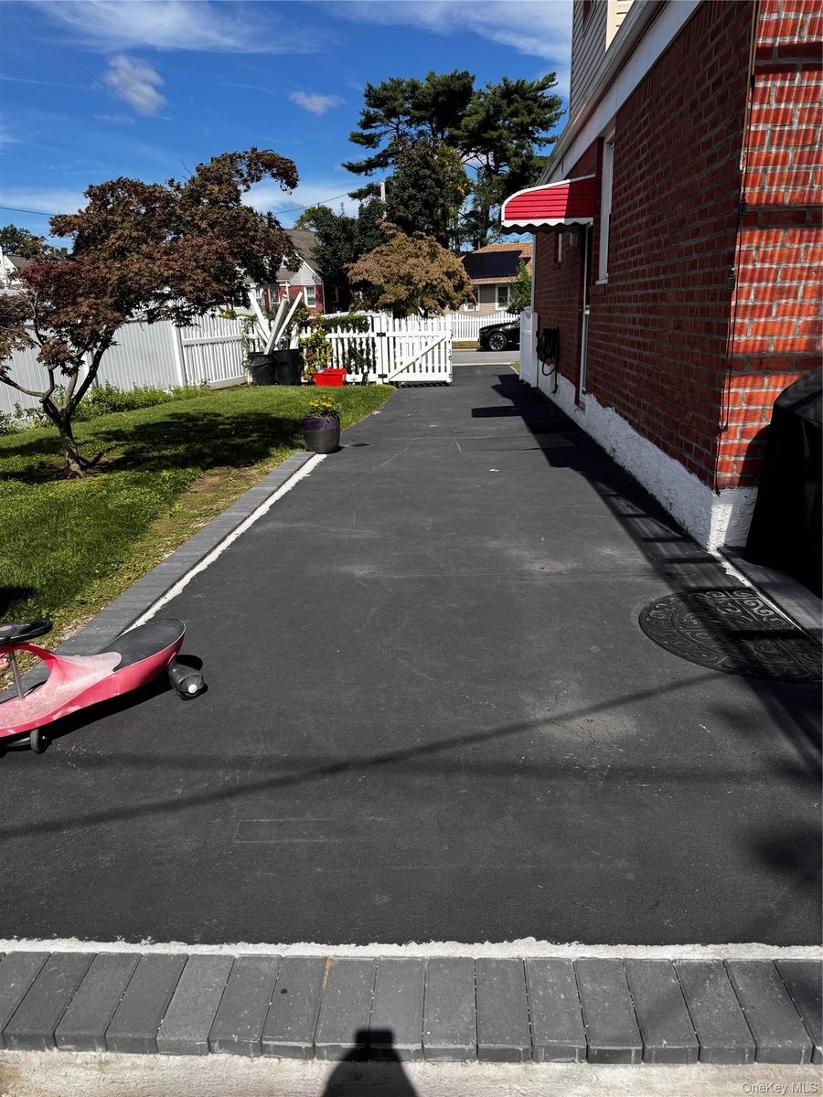 Brick exterior with a red fabric awning, asphalt driveway, and a white picket fence