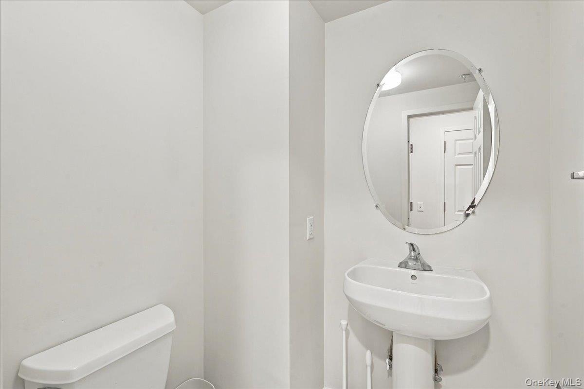 Pedestal sink, wall-mounted oval mirror, and white toilet