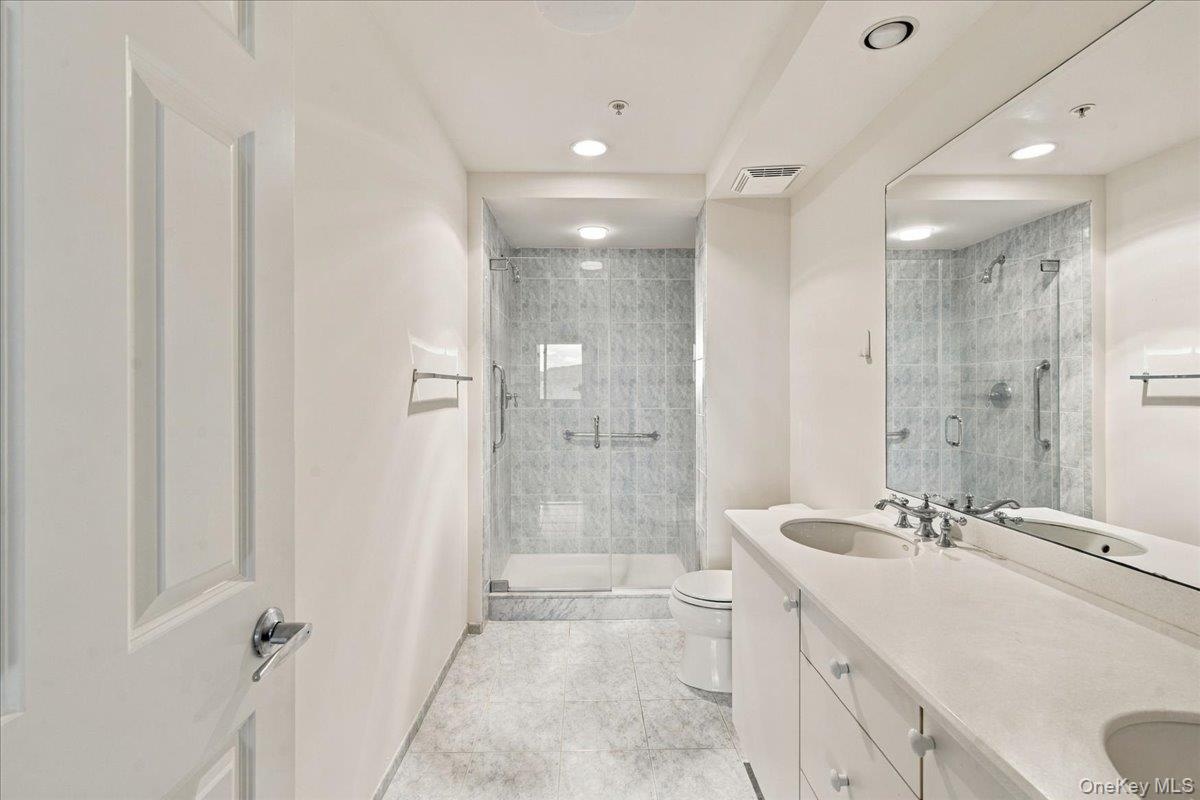 Double vanity with integrated sinks, frameless mirrored wall, glass-enclosed shower, tiled shower walls, and recessed lighting