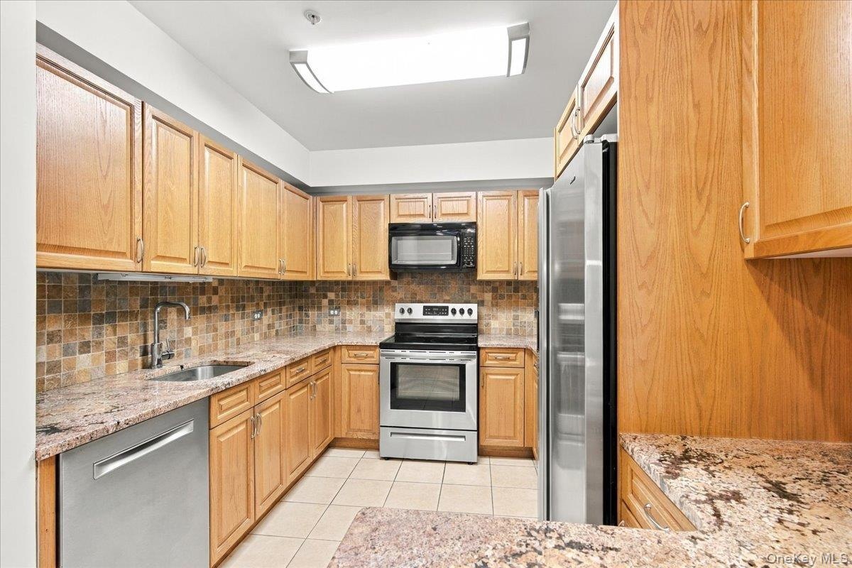 Kitchen featuring wood cabinetry, stainless steel appliances, tiled backsplash, and stone countertops