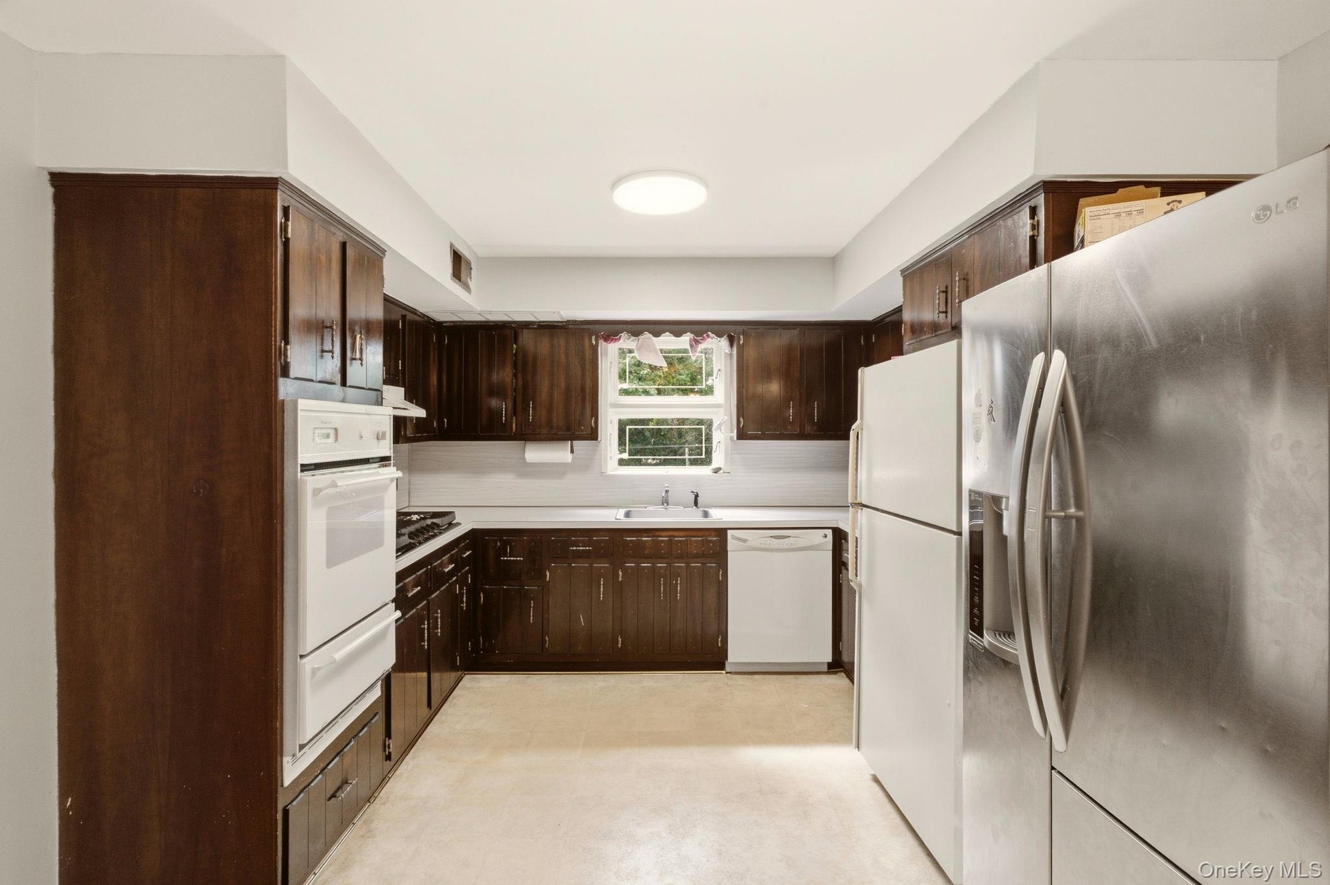 Dark wood-finish cabinetry, white countertop, built-in double oven, and a circular ceiling light fixture
