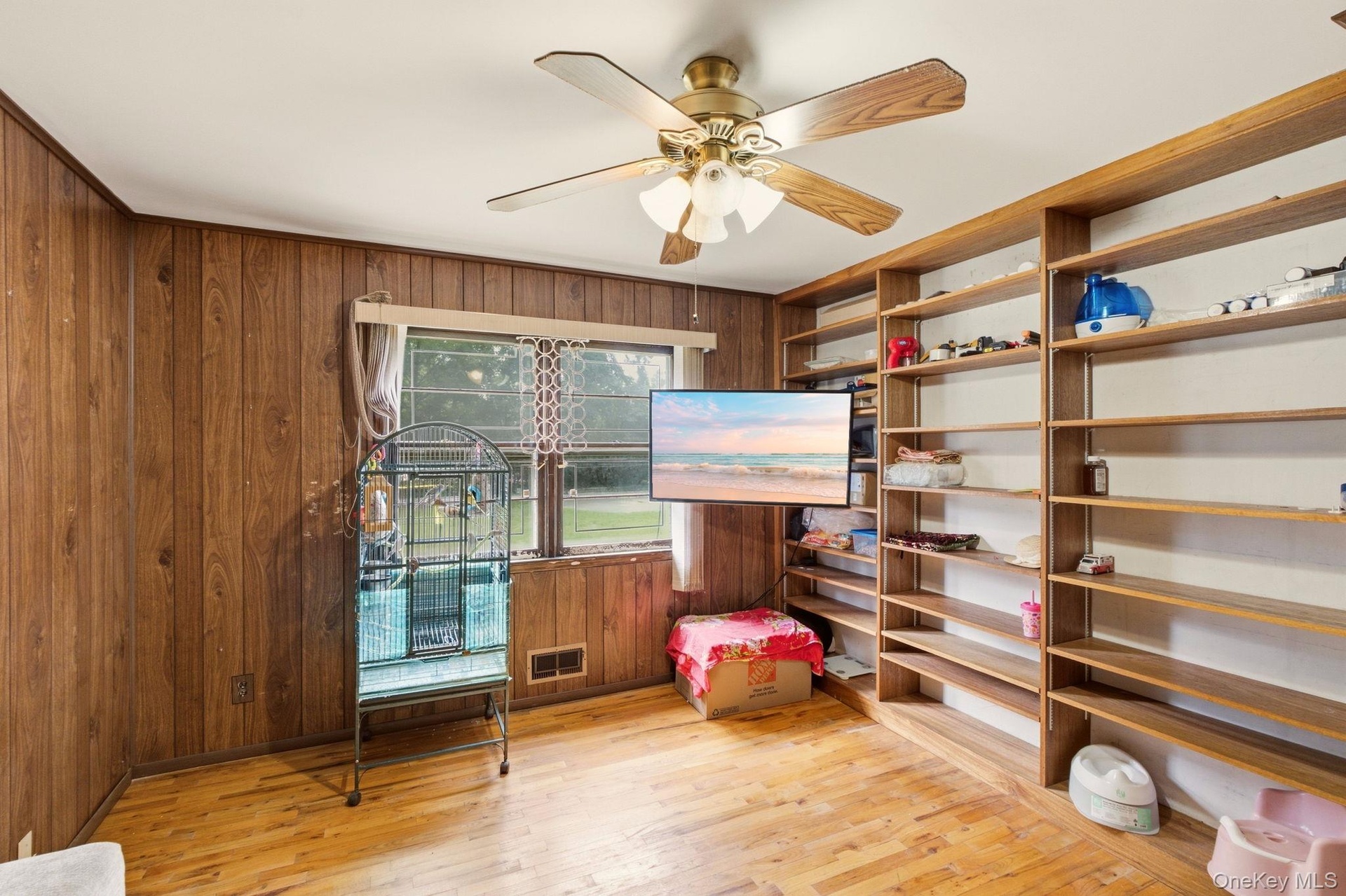 Wood-finish flooring, wood paneling, built-in shelving, ceiling fan with light fixture, and window with natural light
