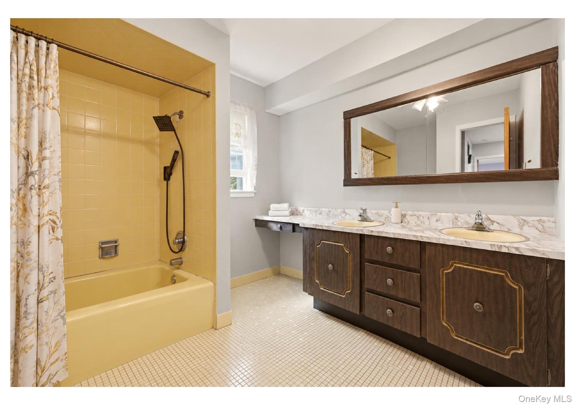 Dual-sink vanity with a marbelized countertop, wood-finish cabinetry, and a large framed mirror