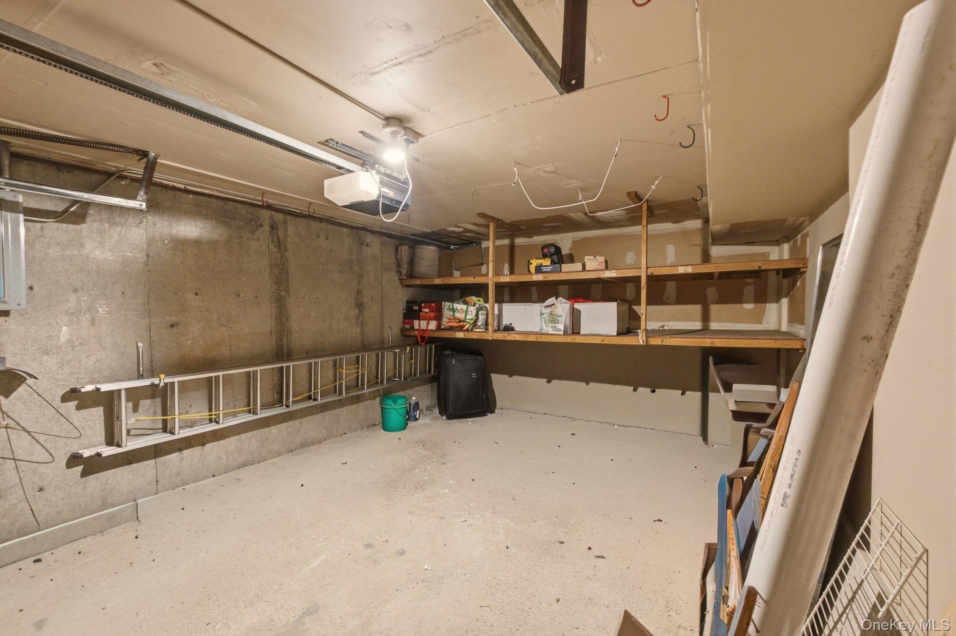 Garage space featuring concrete walls, built-in wooden shelving, and an overhead garage door mechanism