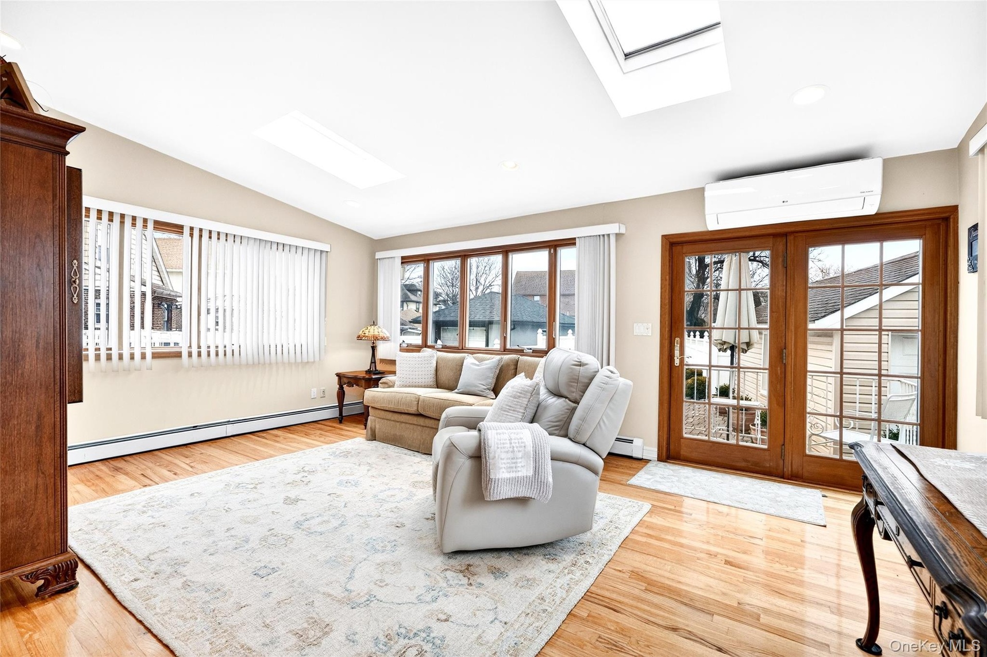 Living area with a skylight, a baseboard radiator, lofted ceiling, a wall mounted AC, and plenty of natural light