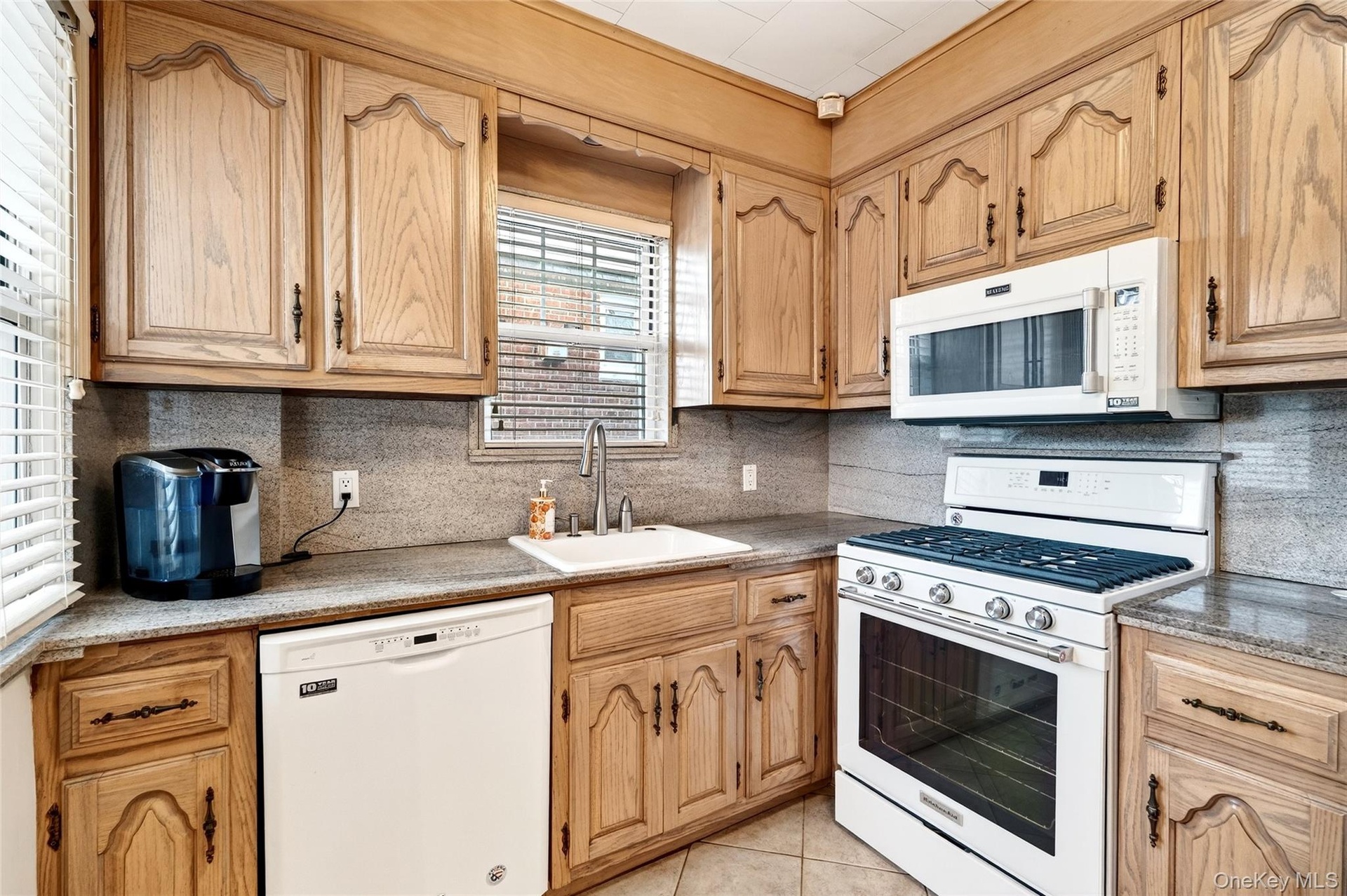 Kitchen featuring white appliances, tasteful backsplash, light tile patterned floors, and light stone counters