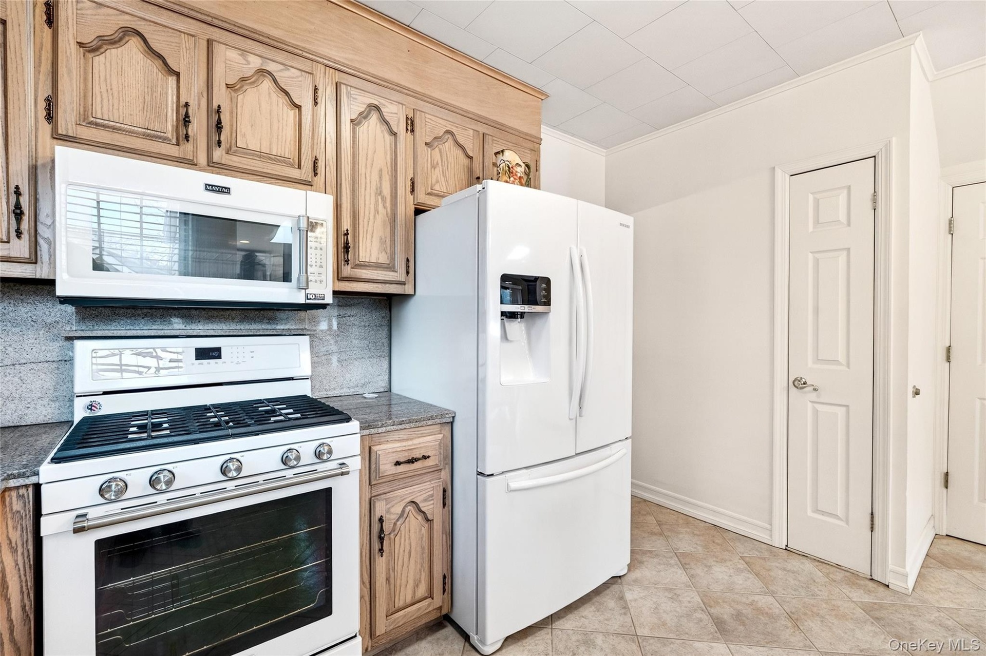 Kitchen featuring white appliances, ornamental molding, backsplash, dark stone countertops, and light brown cabinetry